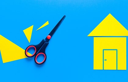 scissors with yellow paper cut-outs that make the shape of a house on a bright blue background
