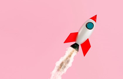 Toy rocket ascending with a plume of smoke on a pink background