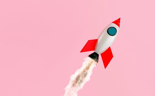 Toy rocket ascending with a plume of smoke on a pink background